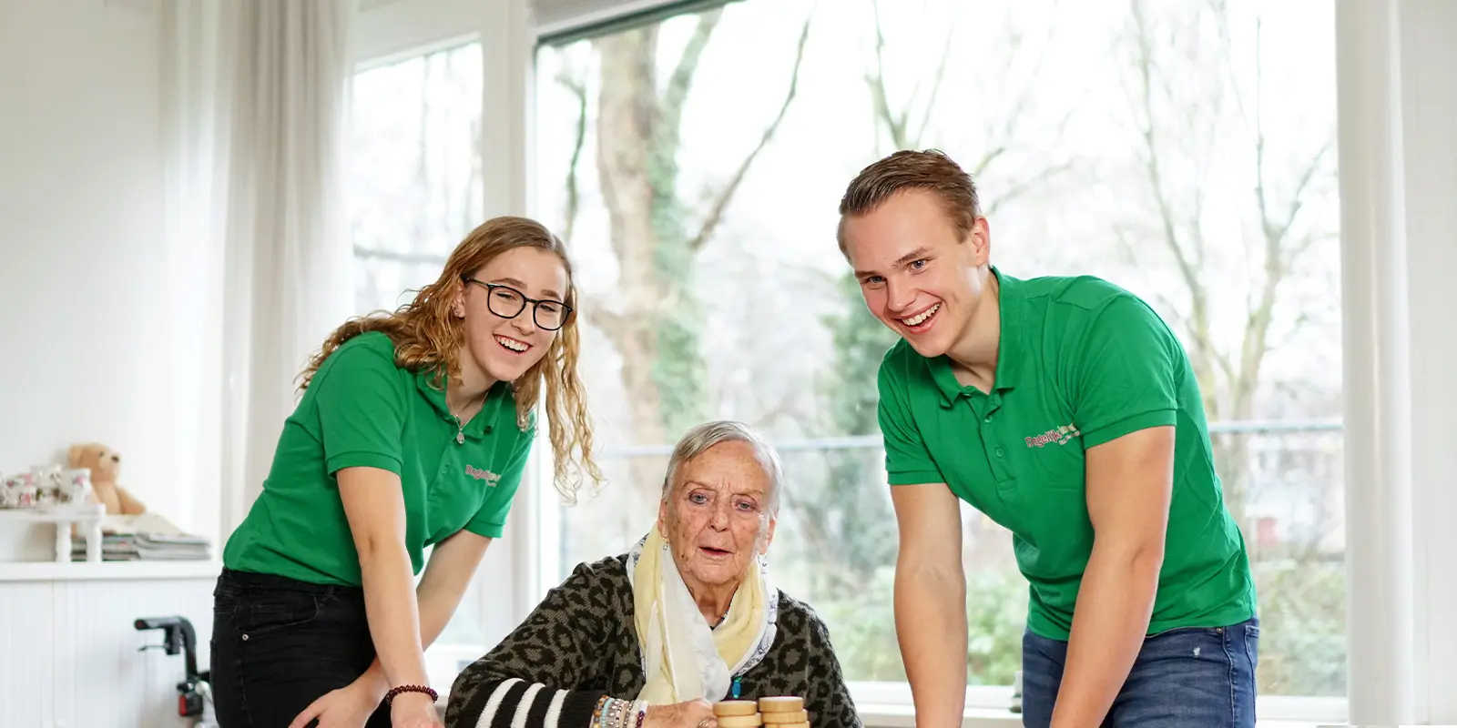 twee studenten doen vakantiewerk bij Dagelijks Leven en sjoelen met een bewoner met dementie.