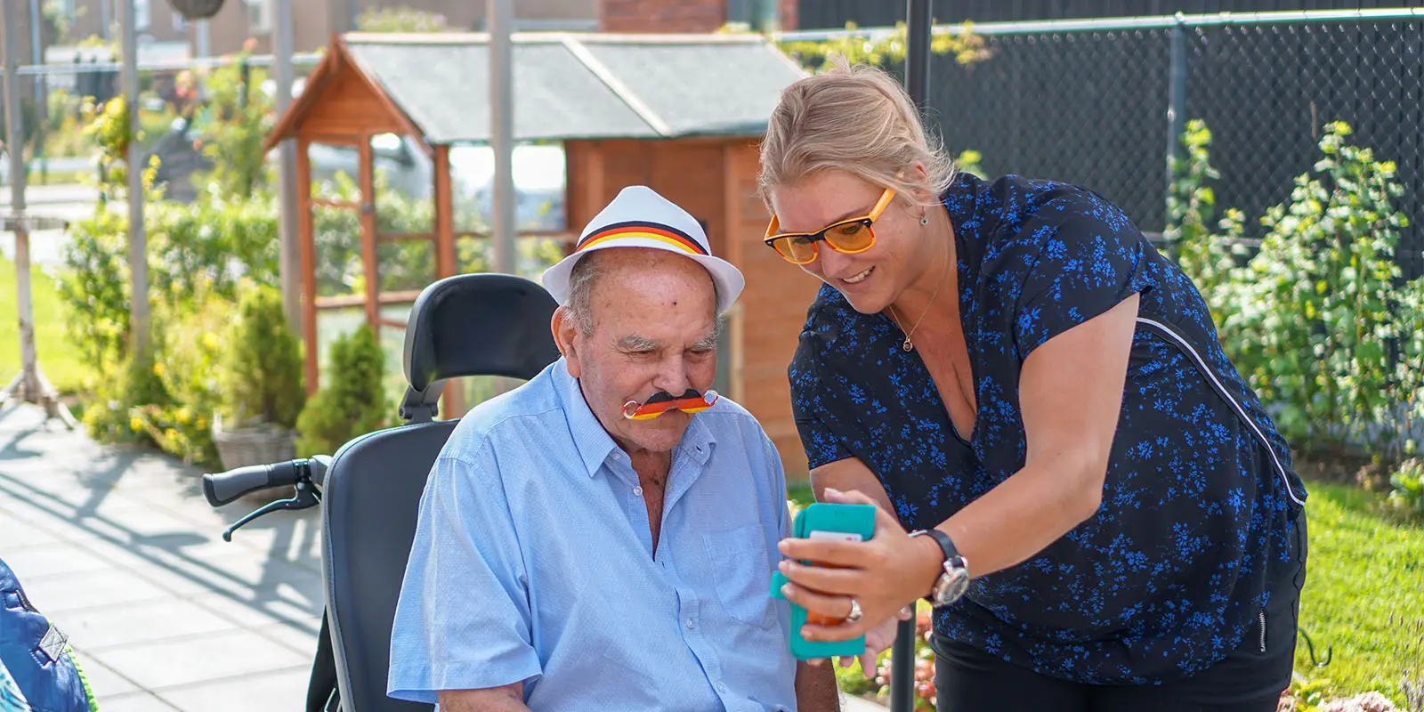Een bewoner met dementie kijkt samen met de locatiemanager op de telefoon wat er geregeld moet worden.