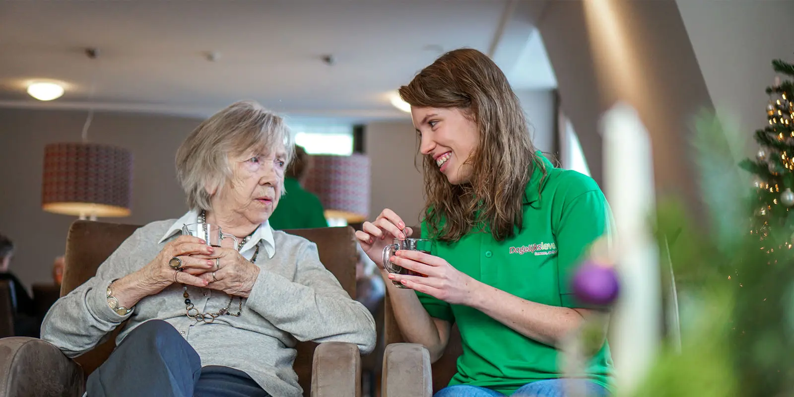Een bewoner met dementie en collega van Dagelijks Leven drinken samen thee en nemen het nieuws door