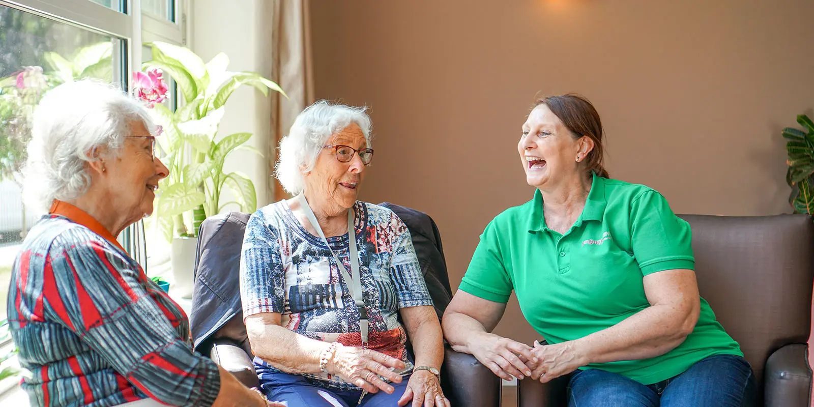 Een locatiemanager kletst en lacht met twee bewoners in een kleinschalige setting, zoals de missie en visie van Dagelijks Leven aangeeft.