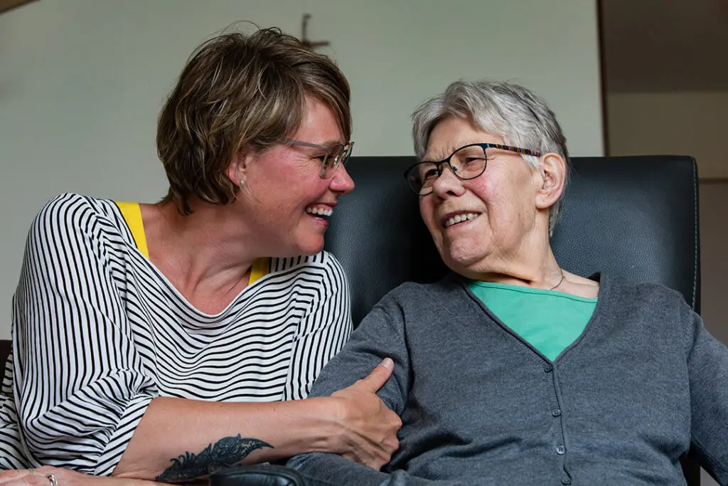 Hetty en haar moeder met dementie knuffelen op de bank bij Dagelijks Leven
