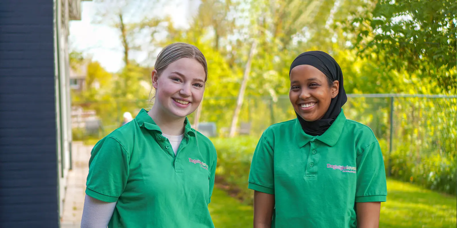 Twee bbl medewerkers van Dagelijks Leven staan samen op de foto in de tuin van hun werkleerplek waar mensen met dementie kleinschalig wonen en waar zij hun leerwerktraject volgen
