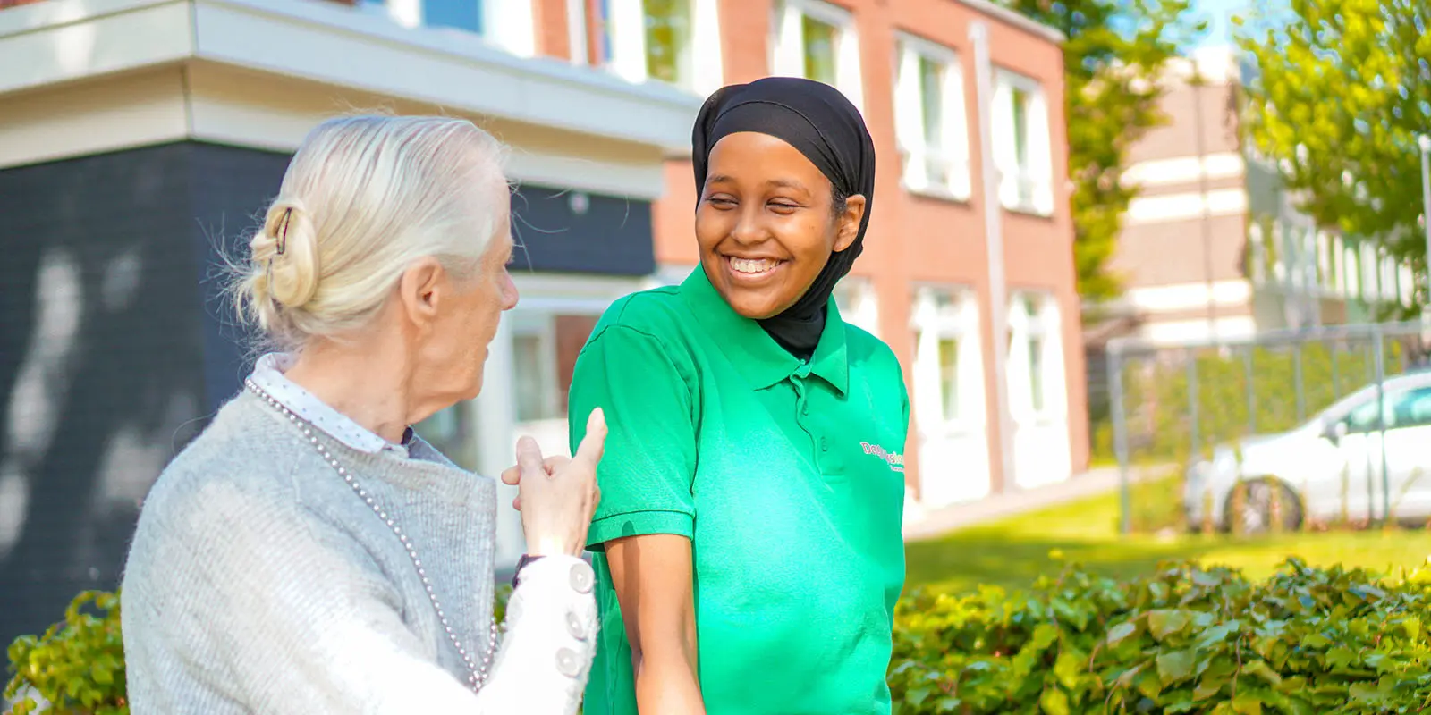 Een bol medewerker van Dagelijks Leven loopt samen met een bewoonster met dementie tijdens haar stage door de tuin van haar stageplek