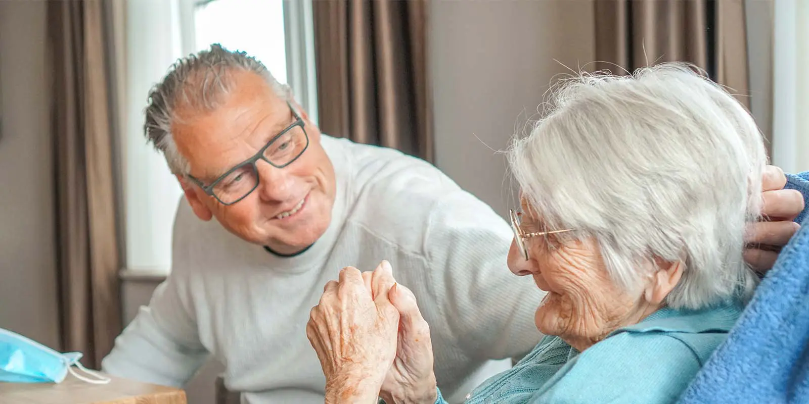 Zoon kijkt naar zijn moeder met vergevorderde dementie, die woont bij Dagelijks Leven. Ze lachen naar elkaar.