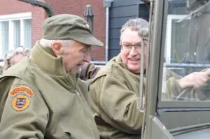 Bewoner met dementie zit samen met zoon in een legervoertuig.