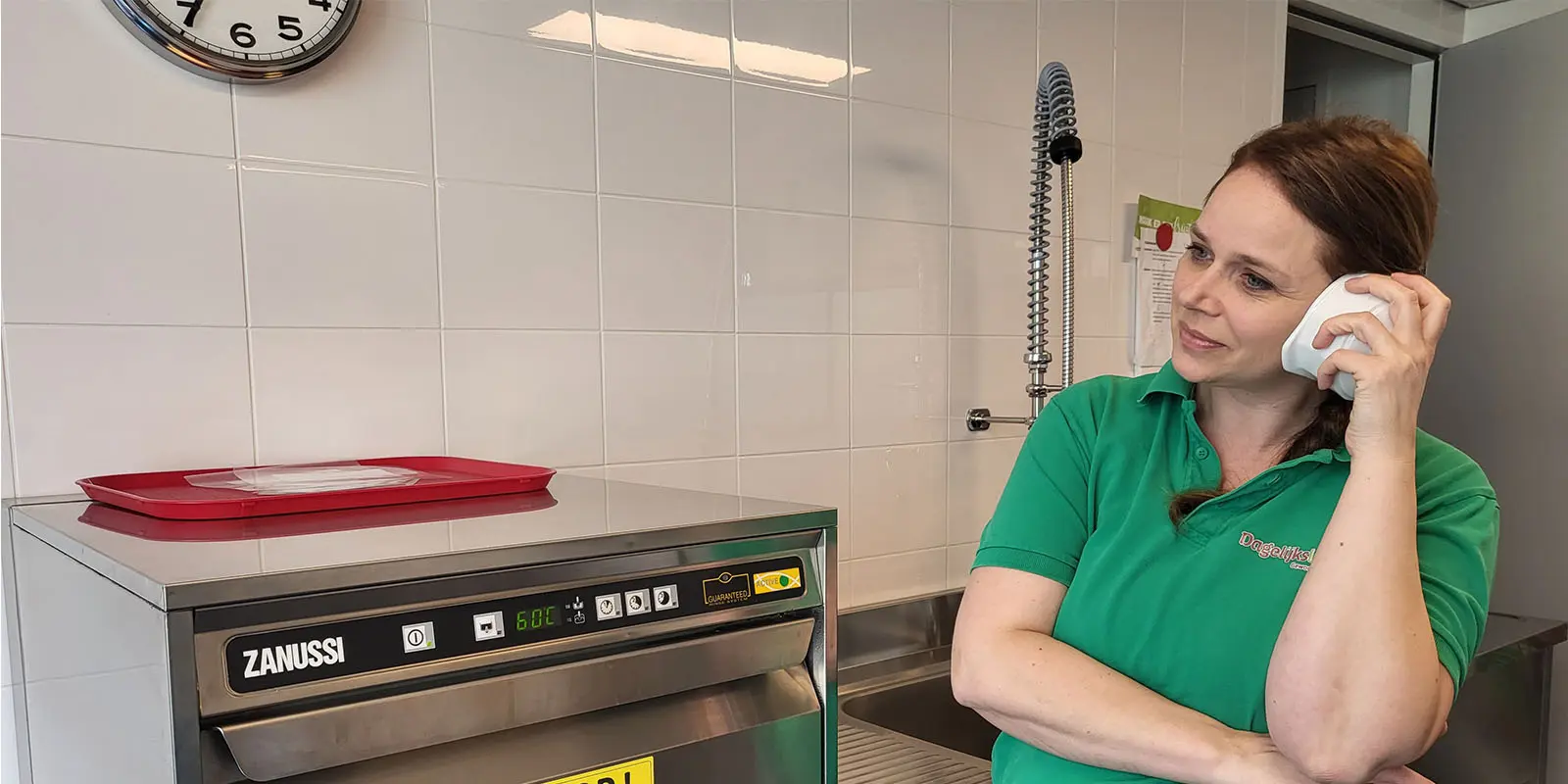 GVP Isabel bij de afwasmachine in de keuken van een woonzorglocatie voor mensen met dementie van Dagelijks Leven, met een soepkom aan haar oor.
