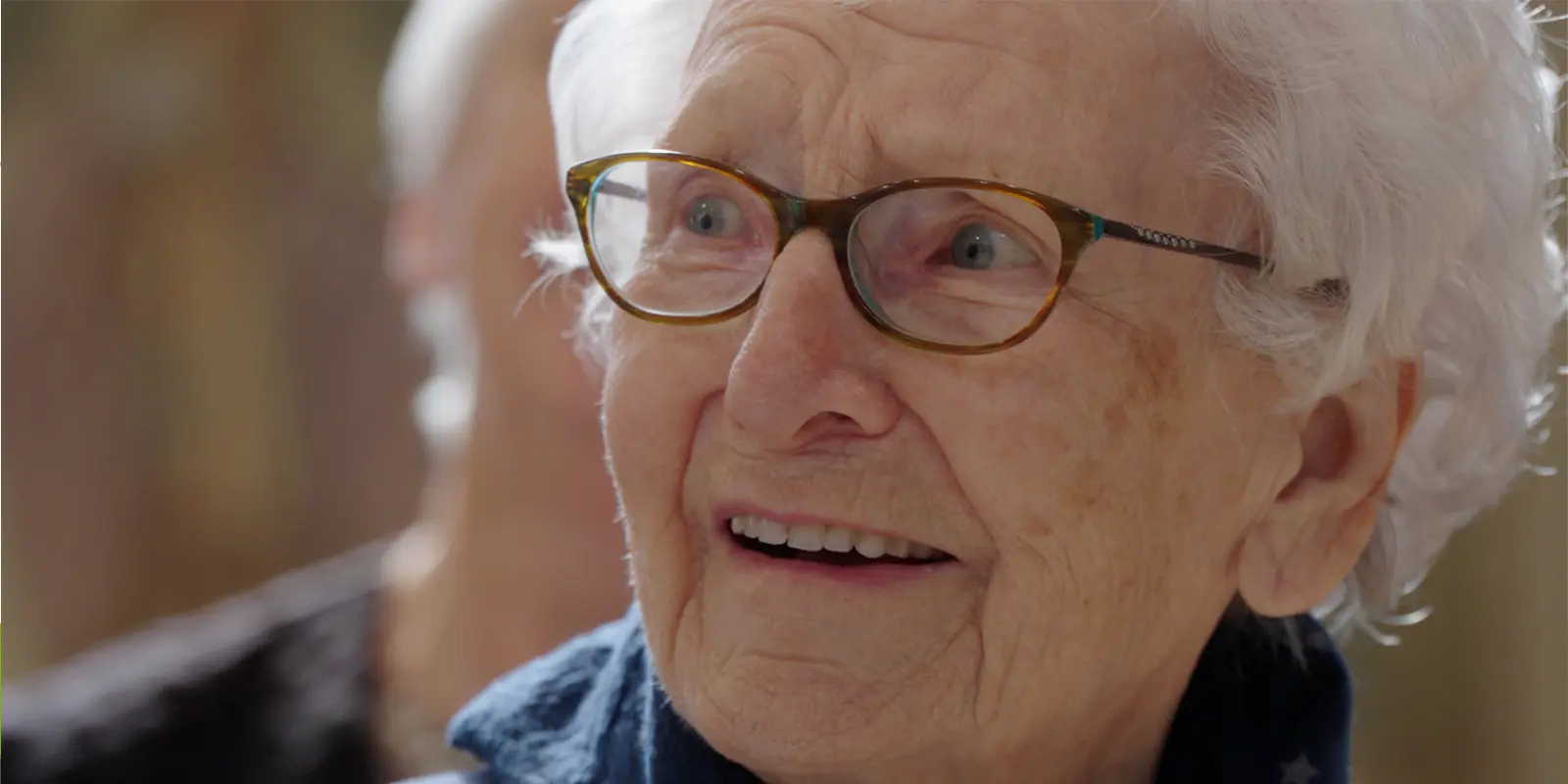 De bewoonster met als hartenwens had om nog eens terug te gaan naar haar doopkerk, kijkt lachend naar een van haar jeugdvriendinnen, die ze daar ook weer ontmoet.