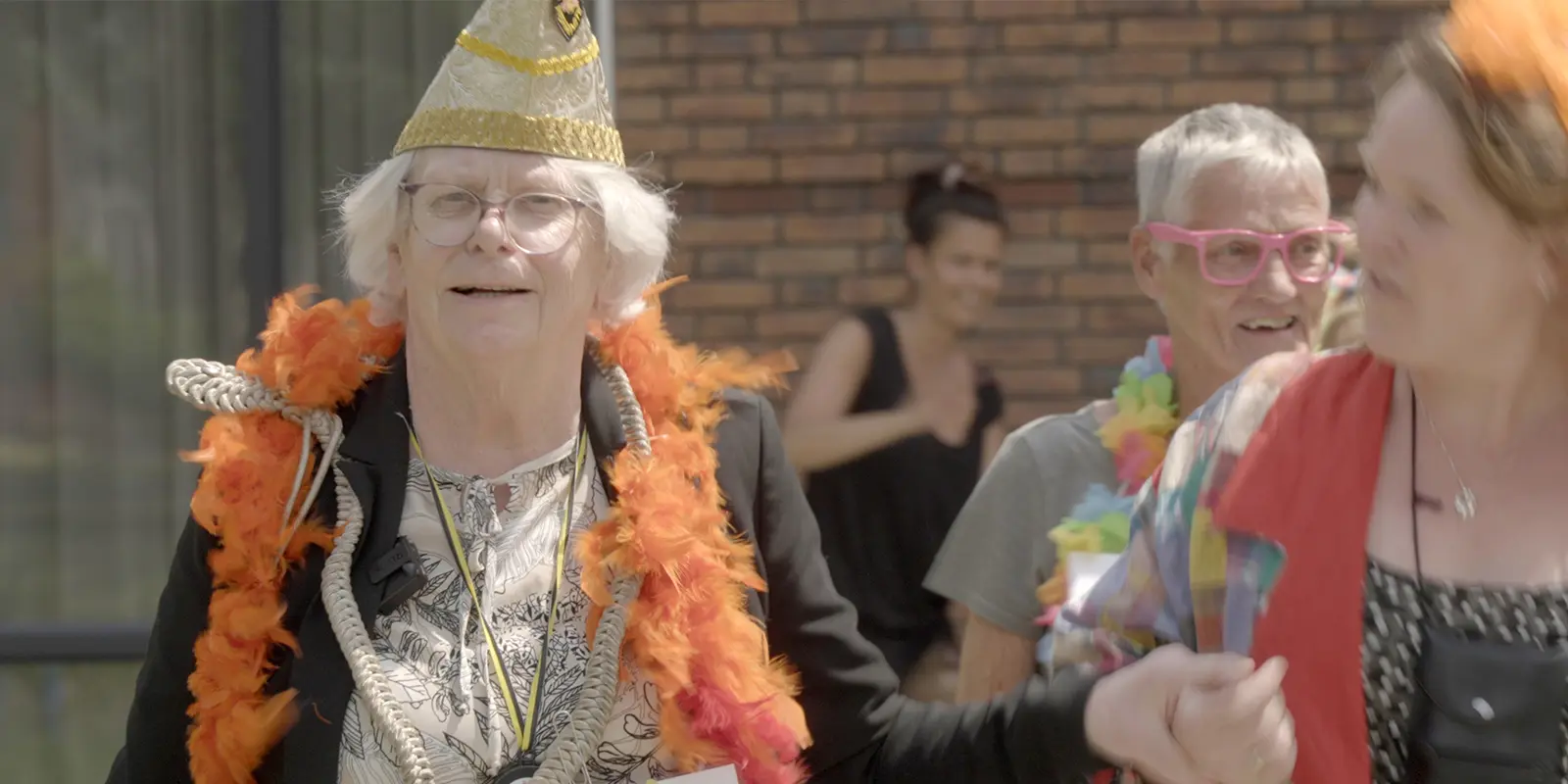 Wil met steek op en kleurige boa om in de polonaise tijdens haar eigen carnaval bij de kleinschalige woonzorglocatie voor dementie, waar ze woont.