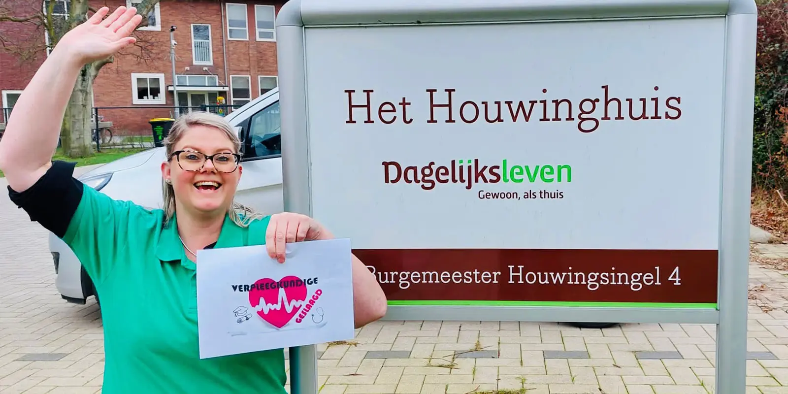 Kelly staat met een bordje 'Verpleegkundige, geslaagd!' voor HEt Houwinghuis, ze steekt vrolijk haar hand in de lucht. Kelly heeft veel geleerd tijdens de twee jaar durende opleiding, maar leert toch het meest in het contact met de bewoners met dementie van Het Houwinghuis.
