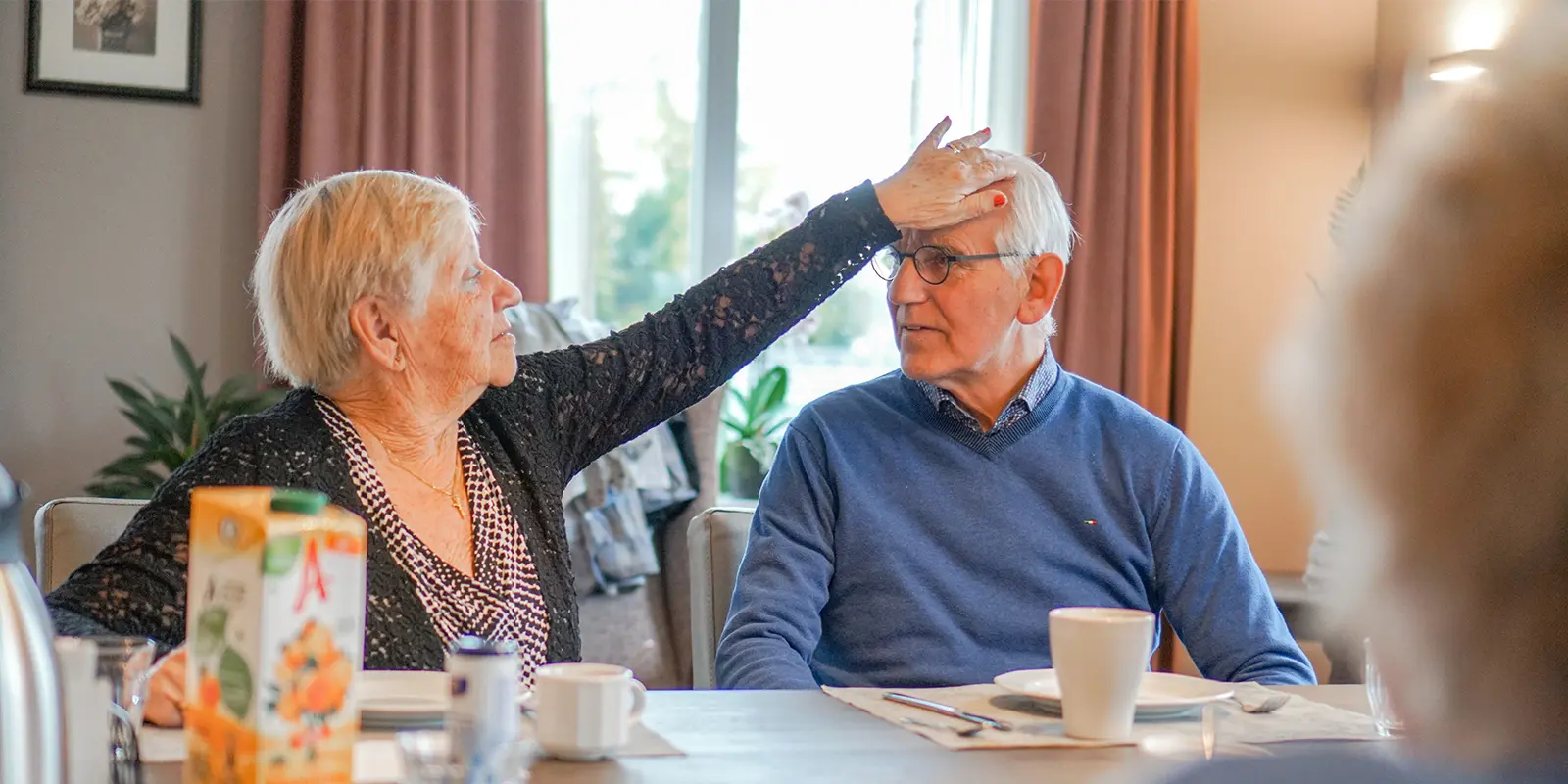 Aan tafel in de zorglocatie voor mensen met dementie vormen medewerkers en bewoners net een groot gezin, vertelt verzorgende IG in deze blog. Foto ter illustratie: twee bewoners aan tafel in een zorglocatie van Dagelijks Leven.