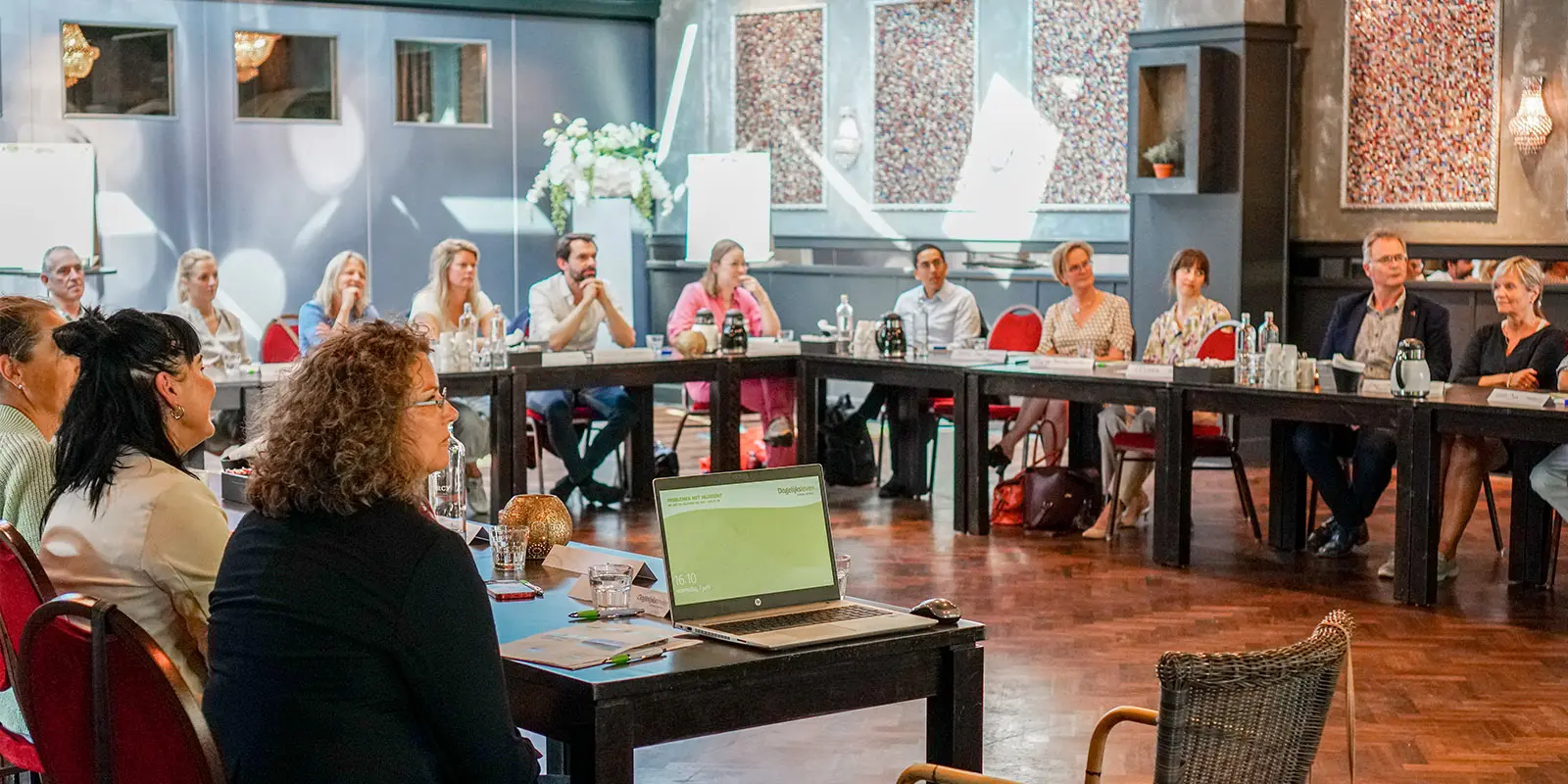 Rondetafelgesprek over de toekomst van medisch-generalistische zorg in kleinschalige, geclusterde ouderenzorg. We zien de aanwezigen aan tafel zitten en luisteren naar Marcel Canoy, die spreekt.