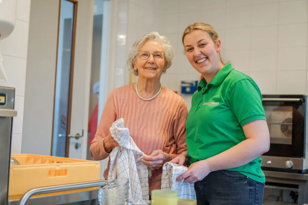 Een bewoonster met Alzheimer en een medewerkster doen samen de afwas in een zorglocatie van Dagelijks Leven.