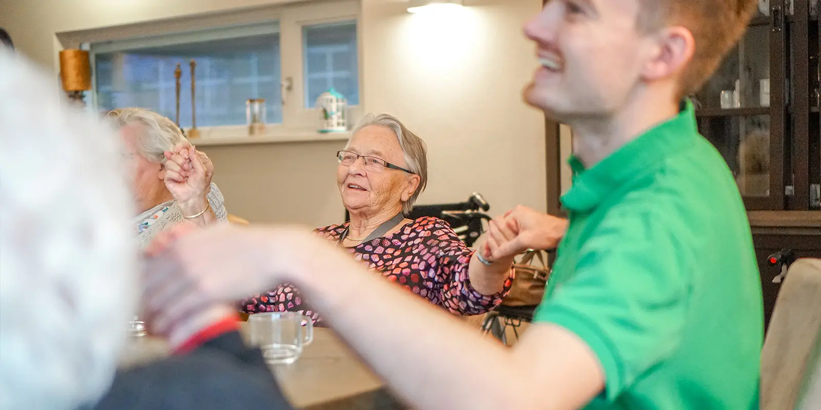 Muziek brengt herinneringen boven water. Soms mooi, soms verdrietig. Als activiteitenbegeleider in de zorg voor mensen met dementie weet onze blogger daar alles van. Foto ter illustratie van bewoners die samen met een medewerker van Dagelijks Leven aan tafel genieten van muziek.