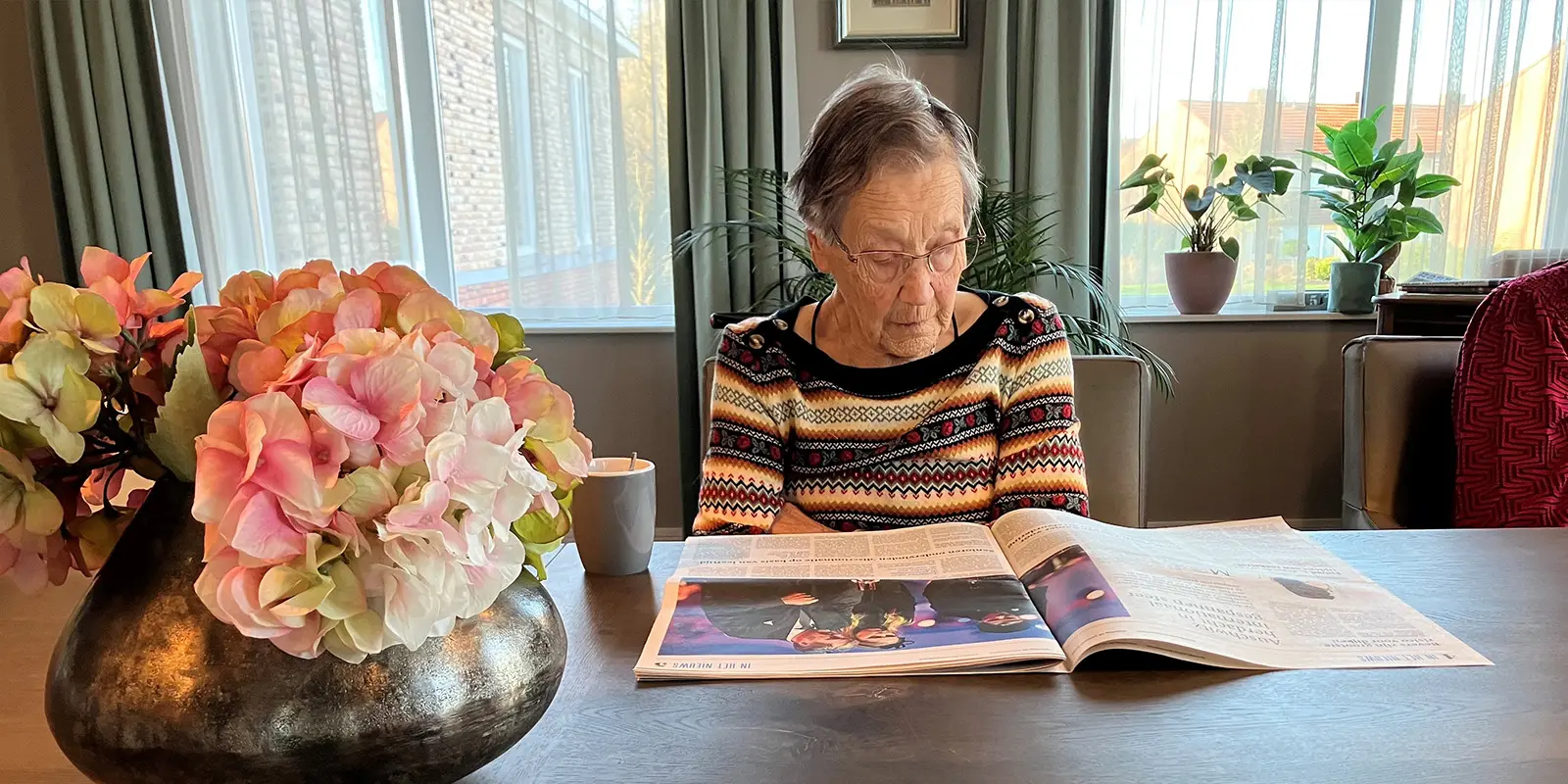 Als gastvrouw in de dementiezorg beleef je op een dag heel wat. Op de foto een bewoner die de krant leest aan de tafel in de gezamenlijke woonkamer van de kleinschalige woonzorglocatie.