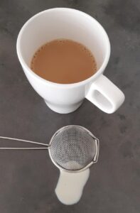 Een kopje koffie met een zeefje en druppels melk ernaast.