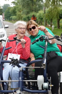 Een bewoner met dementie samen met een zorgmedewerkerp op de duofiets tijdens een sponsortocht bij Dagelijks Leven. 