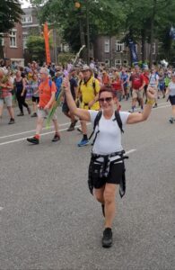 Verpleegkundige Jikkie juichend op de foto terwijl ze de Vierdaagse in 2019 loopt. Dit jaar wandelt ze om geld in te zamelen voor een BeleefTv voor de bewoners met dementie.